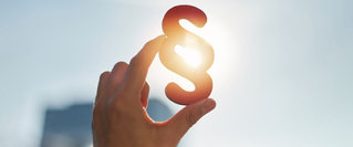 Paragraphen-Symbol wird gegen das Sonnenlicht gehalten – symbolisiert die gesetzlichen Änderungen für 2026 im Bereich Finanzen.