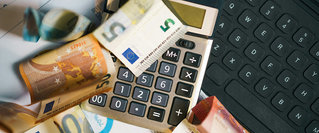 Euro-Geldscheine liegen verstreut neben einem Taschenrechner und einer Computertastatur. Die Szene vermittelt den Eindruck eines finanziellen Überblicks oder einer Budgetplanung – passend zum Check-up von Finanzen und Verträgen zum Jahreswechsel 2026.