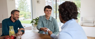 Ein junger Mann überreicht im Beisein seines Vaters Unterlagen an einen Finanzcoach der DVAG – persönliche Beratung zum Berufseinstieg, zur Ausbildung und zu finanziellen Fragen rund um den Start ins Berufsleben.