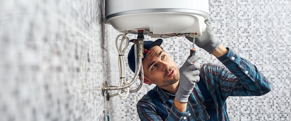 Ein Handwerker installiert einen Warmwasserspeicher in einem Wohnhaus – Symbolbild für den Austausch von Heizungsanlagen und die neuen gesetzlichen Vorgaben des Gebäudemodernisierungsgesetzes für Eigentümer und Vermieter.