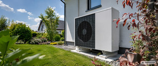 Außeneinheit einer Wärmepumpe an der Fassade eines Einfamilienhauses mit gepflegtem Garten – Symbolbild für die staatliche Förderung von Wärmepumpen und die Modernisierung energieeffizienter Heizsysteme.