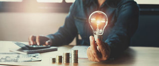 Darstellung von Finanzwissen und Inflation: Gestapelte Münzen und eine leuchtende Glühbirne symbolisieren Geldsparen und clevere Strategien gegen steigende Preise.