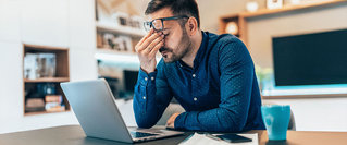 Gestresster Mann sitzt erschöpft vor dem Laptop – Symbolbild für Burnout, mentale Belastung und die Notwendigkeit von Prävention.