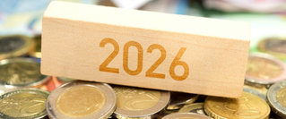 Holzklotz mit der Aufschrift ‚2026‘ liegt auf gestapelten Euro-Münzen und symbolisiert Finanzplanung, Kosten oder wirtschaftliche Entwicklungen im Jahr 2026.